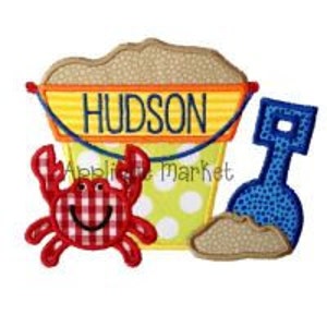 May include: A red and white checkered crab, a yellow bucket with the name "HUDSON" on it, and a blue shovel with sand on it. The bucket has yellow polka dots and a yellow and orange striped handle.