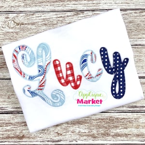 Puede incluir: Tela blanca con el nombre "Lucy" bordado en rojo, blanco y azul. Las letras están en una fuente juguetona, con la "L" y la "Y" en un estampado de cachemira y la "U" en un estampado de cuadros. La "C" tiene un estampado de rayas. El logotipo de Applique Market está en la parte inferior derecha.