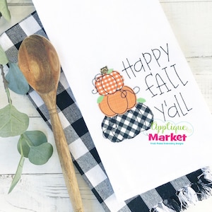 May include: White kitchen towel with a stack of three embroidered pumpkins and the text "Happy Fall Y'all" in black cursive. The bottom pumpkin is black and white checkered, the middle pumpkin is orange, and the top pumpkin is orange and white checkered. The text "Applique Market Fresh Picked Embroidery Designs" is also embroidered in black.