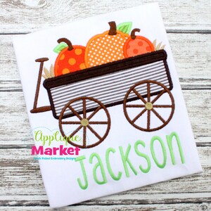 May include: A brown wagon with wheels and a handle, filled with three orange pumpkins with white polka dots. The wagon is on a white background with the name "Jackson" written in green below it.