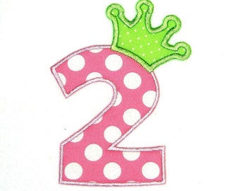 May include: Pink number two with white polka dots and a green crown on top. The number is outlined in white.