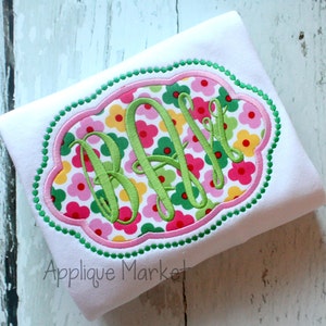 May include: A white t-shirt with a green, pink, and yellow floral monogram design in a scalloped frame. The monogram is "B.F.L."