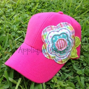 May include: A pink baseball cap with a large multi-colored fabric flower applique. The flower has a pink and white striped center, a turquoise blue center with white polka dots, and layers of green, pink, and white fabric.