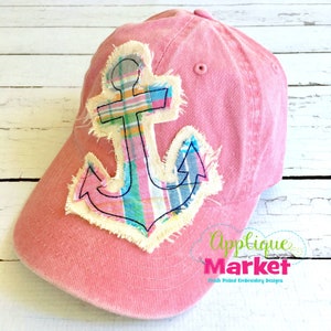 May include: A pink baseball cap featuring a large anchor applique. The anchor is crafted from white fabric with a plaid pattern in pink, blue, and yellow. The anchor is outlined in black thread and has a frayed edge.