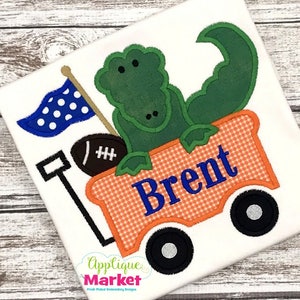 May include: A green alligator riding in a red and orange wagon with a blue and white flag, a football, and the name "Brent" on the side.
