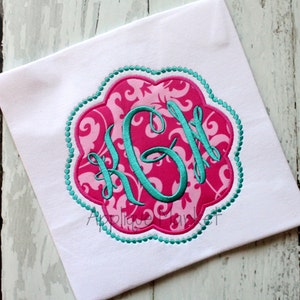 May include: A pink and teal monogram with the letters "KGH" embroidered on a white fabric background.