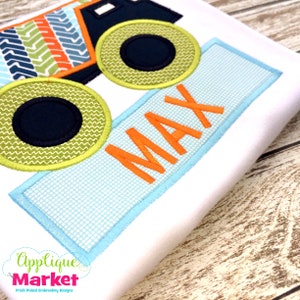 May include: A green, orange and blue monster truck applique with black wheels. The truck is next to a blue rectangle with the name "MAX" in orange letters.