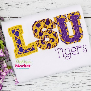 May include: A white t-shirt with a purple and yellow applique of the letters "LSU" with the word "Tigers" underneath.