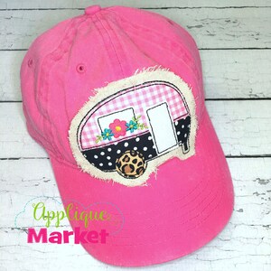 May include: Pink baseball cap with a white, black and pink embroidered camper applique featuring a floral design. The camper has a gingham pattern and a leopard print tyre.
