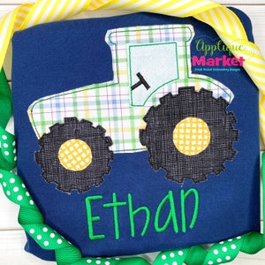 May include: A blue shirt with a green and yellow tractor applique and the name "Ethan" embroidered in green.