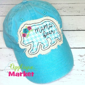 May include: A turquoise blue baseball cap with a white applique of a bear with the text "mama bear" in black lettering. The bear has a pink and blue floral design on its head.