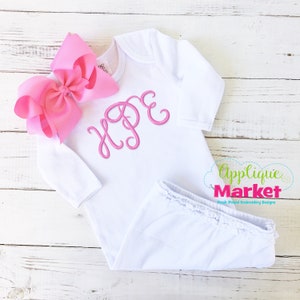 May include: White baby onesie with long sleeves and a pink embroidered name "HOPE". The onesie has a ruffled bottom and is paired with a large pink bow.