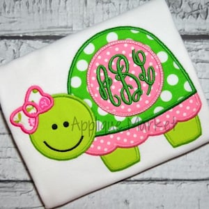 May include: Green and pink applique of a turtle with a pink bow and a pink circle with white polka dots and green embroidered initials "A.B.D."