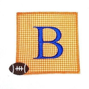 May include: A blue letter "B" embroidered on a square of orange and white gingham fabric. A brown football with white laces is in the bottom left corner.