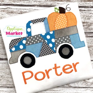 Puede incluir: Un camión de patchwork azul y gris con una calabaza en la caja. El camión tiene ruedas negras y una ventana blanca. El nombre "Porter" está bordado en naranja debajo del camión.
