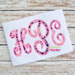 May include: A white t-shirt with a pink and blue monogram of the letters "HPE" in a script font. The letters are filled with a paisley pattern and outlined in pink. The text "Applique Market" is in the bottom right corner of the shirt.