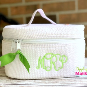 May include: White oval-shaped cosmetic bag with a zipper closure and a green ribbon pull. The bag has a green monogram "MRP" embroidered on the front.