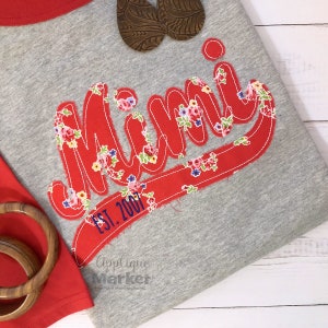 Peut inclure: Appliqué en tissu floral rouge et blanc sur un t-shirt gris avec le mot "Mimi" en écriture rouge et le texte "Est. 2001" en écriture bleue.