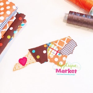 May include: A patchwork design of North Carolina in various colors and patterns, including brown, orange, white, and blue. The design includes a small pink heart in the lower left corner. The text "Applique Market" is in the lower right corner, with the tagline "Fresh Picked Embroidery Designs".