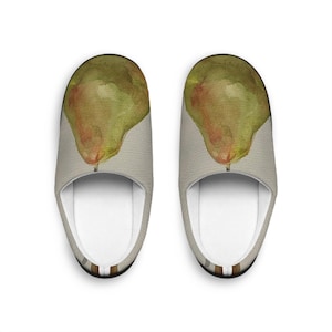 Puede incluir: Un par de zapatillas con un diseño de pera. Las zapatillas muestran una pintura de acuarela de una pera verde con toques rojos y un tallo marrón. El fondo es beige claro, con un interior blanco.