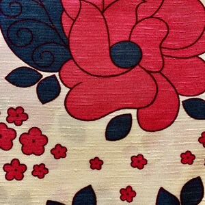 May include: A cream-colored fabric with a repeating pattern of red and blue flowers. The flowers are stylized and have a retro look. The fabric has a textured surface.