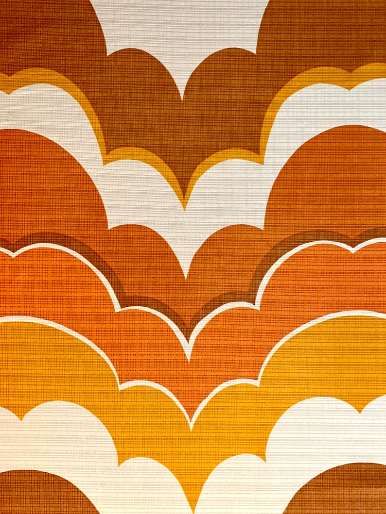 Op de afbeelding: Close-up van een retro behangpatroon. Het ontwerp toont gelaagde, wolkvormige vormen in tinten bruin, oranje en geel, omlijnd met wit. Het gestructureerde oppervlak voegt diepte toe aan het herhalende motief.