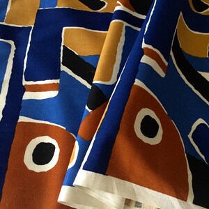 May include: A close-up of a fabric with a geometric pattern in shades of blue, orange, and black. The fabric is folded in half, revealing the white underside.