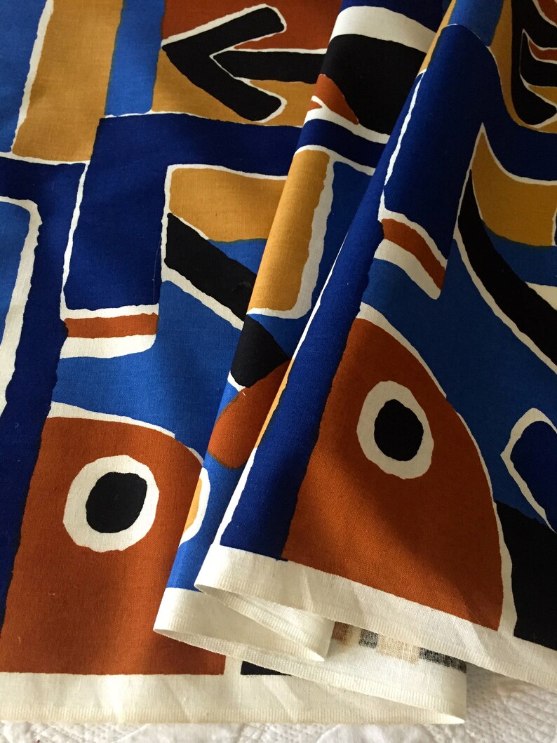 May include: A close-up of a fabric with a geometric pattern in shades of blue, orange, and black. The fabric is folded in half, revealing the white underside.