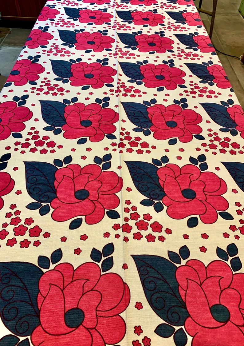 May include: A white fabric with a repeating pattern of large pink flowers with dark blue leaves and small pink flowers.