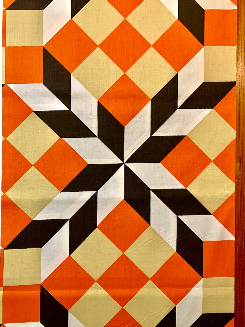 K&ouml;nnte beinhalten: Ein geometrischer Stoff mit einem sich wiederholenden Muster aus orangefarbenen, wei&szlig;en und schwarzen Quadraten. Die Quadrate sind diagonal angeordnet und erzeugen so eine Tiefenwirkung und Bewegung.