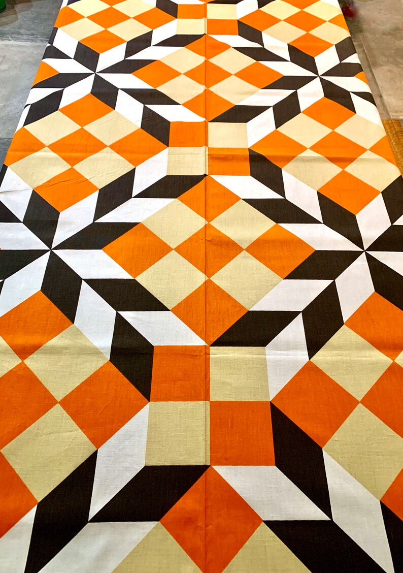 K&ouml;nnte beinhalten: Ein Stoff mit geometrischem Muster in Orange, Wei&szlig;, Schwarz und Beige mit Quadraten und Rauten. Der Stoff hat ein sich wiederholendes Muster aus Quadraten und Rauten.