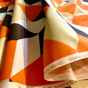 K&ouml;nnte beinhalten: Orangefarbener, schwarz-wei&szlig;er geometrischer Stoff mit dem aufgedruckten Text "DIMENSIONS" und "KANLEY" am Rand. Der Stoff ist gefaltet und der Text ist am Rand der Falte sichtbar.