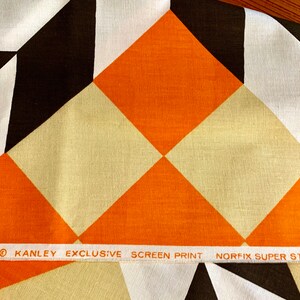 K&ouml;nnte beinhalten: Orangefarbener, wei&szlig;er und brauner geometrischer Stoff mit einem wei&szlig;en Etikett mit der Aufschrift "DIMENSIONS&reg; KANLEY EXCLUSIVE SCREEN PRINT NORFIX SUPER STAIN REPELLENT."