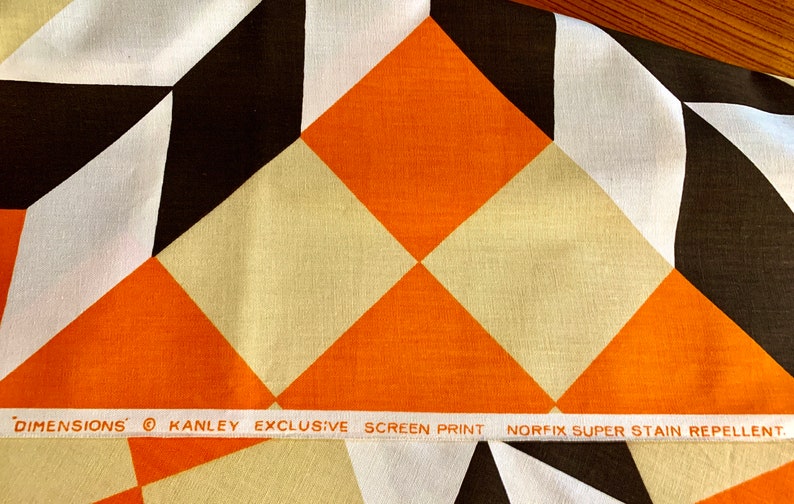 K&ouml;nnte beinhalten: Orangefarbener, wei&szlig;er und brauner geometrischer Stoff mit einem wei&szlig;en Etikett mit der Aufschrift "DIMENSIONS&reg; KANLEY EXCLUSIVE SCREEN PRINT NORFIX SUPER STAIN REPELLENT."