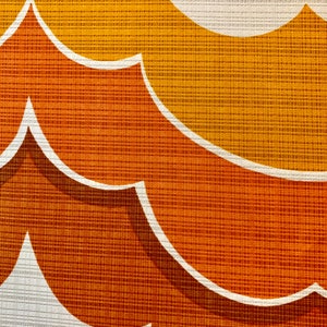Op de afbeelding: Close-up van een retro stof met een herhalend patroon van gestileerde, gebogen vormen. Het ontwerp heeft tinten oranje, geel en wit, waardoor een getextureerd, gelaagd effect ontstaat. De stof heeft een geweven uiterlijk.