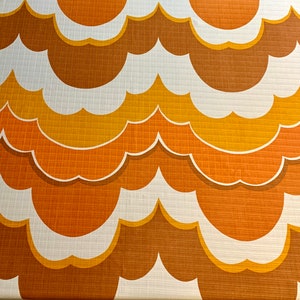 Op de afbeelding: Een stof met een herhalend patroon van gestileerde, wolkvormige vormen in bruin, oranje, geel en wit. Het retro-ontwerp heeft een textuur. De stof is geschikt voor woondecoratie of bekleding.