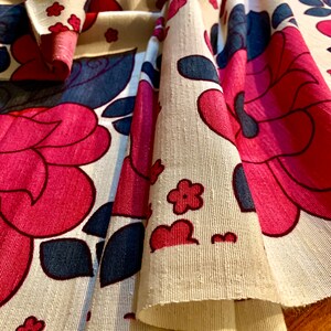 May include: Cream colored fabric with a pink and blue floral pattern. The fabric is folded and the pattern is visible on both sides of the fold.