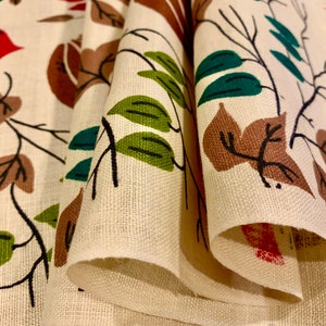 May include: Close-up of a folded fabric with a repeating pattern of brown, green, and red stylized leaves and branches on a white background.