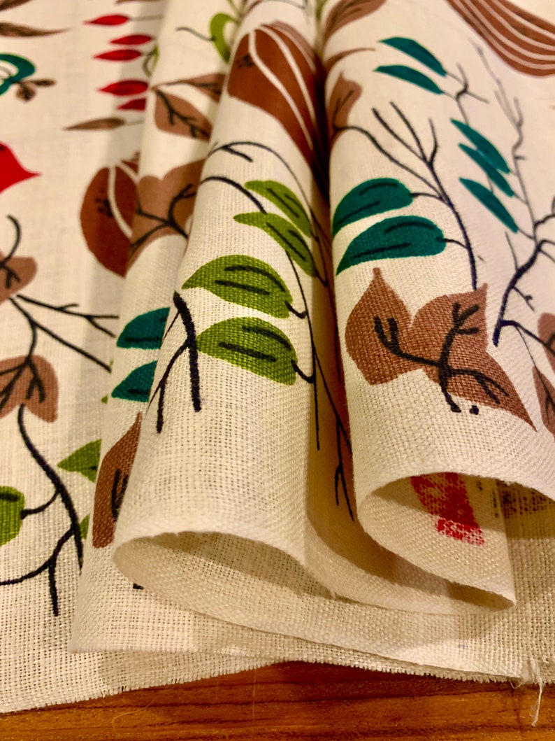 May include: Close-up of a folded fabric with a repeating pattern of brown, green, and red stylized leaves and branches on a white background.