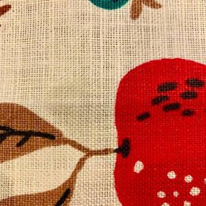 May include: A close-up of a fabric with a red, white, and brown pattern. The fabric has a textured surface and a woven design. The pattern includes a red pear with white dots and a brown leaf.