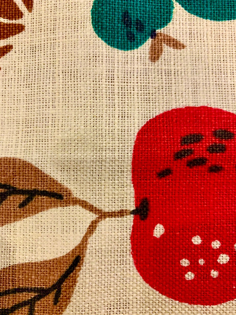 May include: A close-up of a fabric with a red, white, and brown pattern. The fabric has a textured surface and a woven design. The pattern includes a red pear with white dots and a brown leaf.