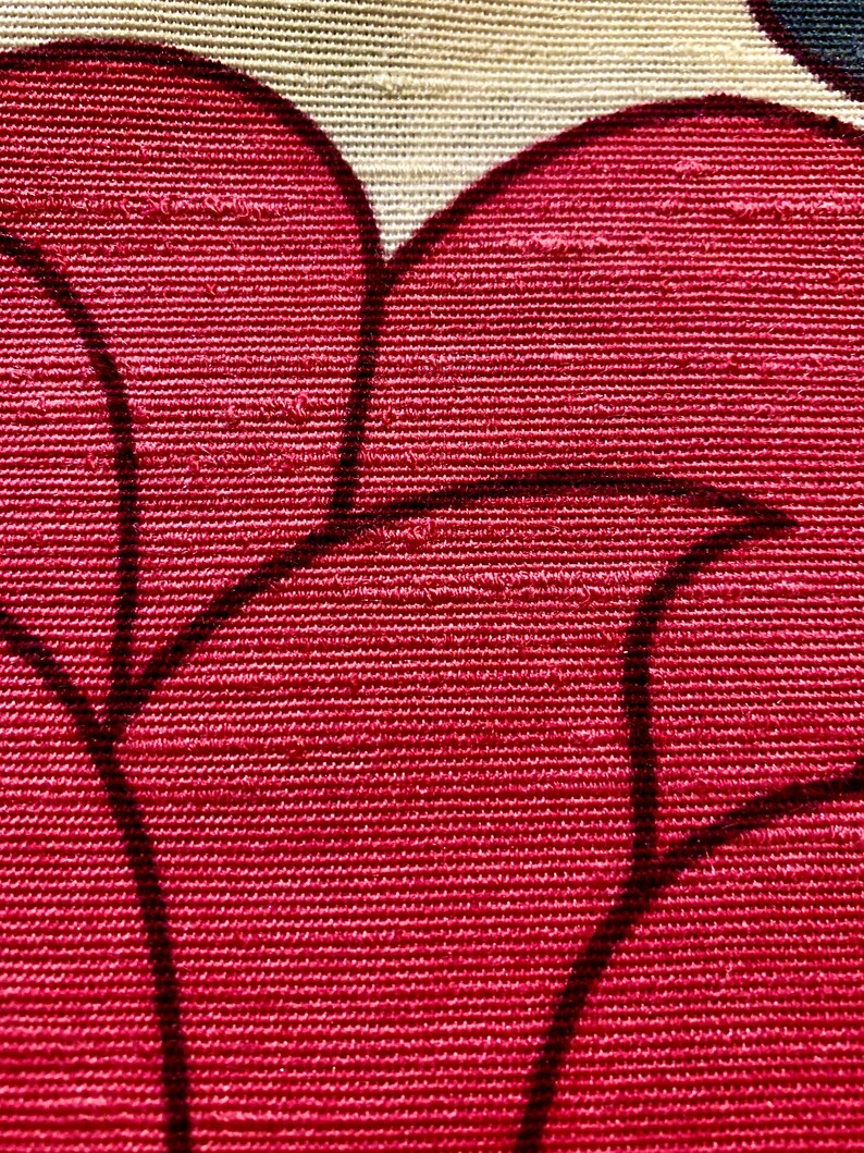 May include: Close-up of a red fabric with a textured weave. The fabric has a black floral pattern.
