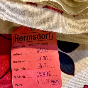 May include: A pink fabric label with black text that reads "Hermsdorf Material: 100% Polyacryl" and includes product information such as "Artikel 8902", "Breite ca. 1.20", "Kontrolle He.T", "St&uuml;ck-Nr. 25492", and "Meter 41.00/409".