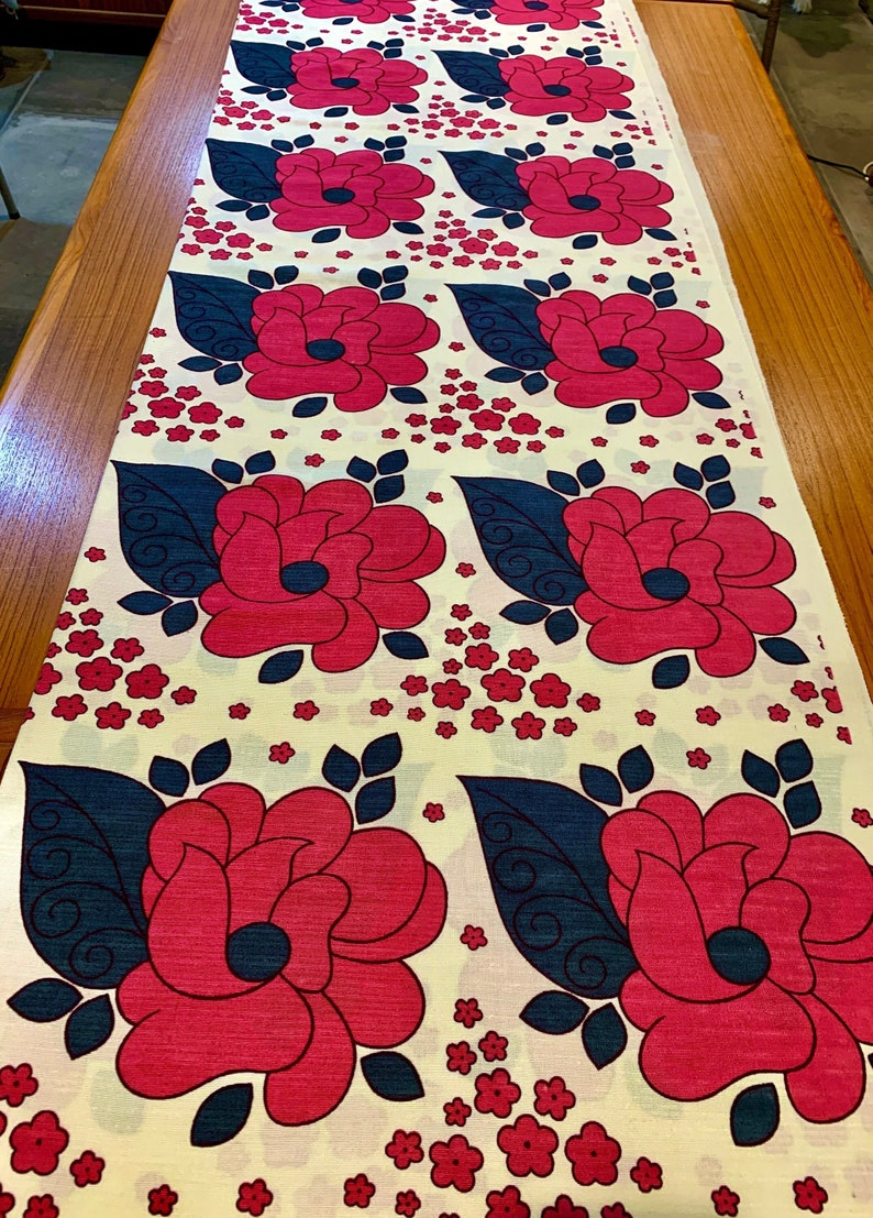 May include: A white fabric with a repeating pattern of large pink flowers with dark blue leaves and small pink flowers.