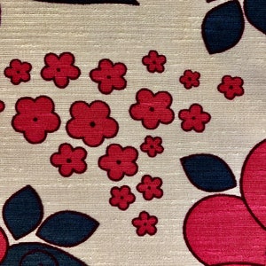 May include: A beige fabric with a repeating pattern of red and blue flowers. The flowers are stylized and have a retro look. The fabric has a textured surface.