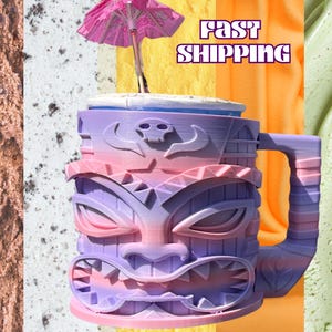 Pode incluir: Uma caneca tiki colorida com uma alça, apresentando um design de rosto esculpido em tons de roxo, rosa e azul. Um pequeno guarda-chuva rosa é colocado em cima da caneca. A caneca é projetada para bebidas tropicais.