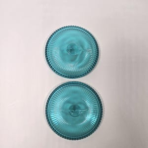 May include: Two turquoise glass plates with a ribbed design and a beaded edge. The plates are round and have a central design element. The plates are displayed on a white background.