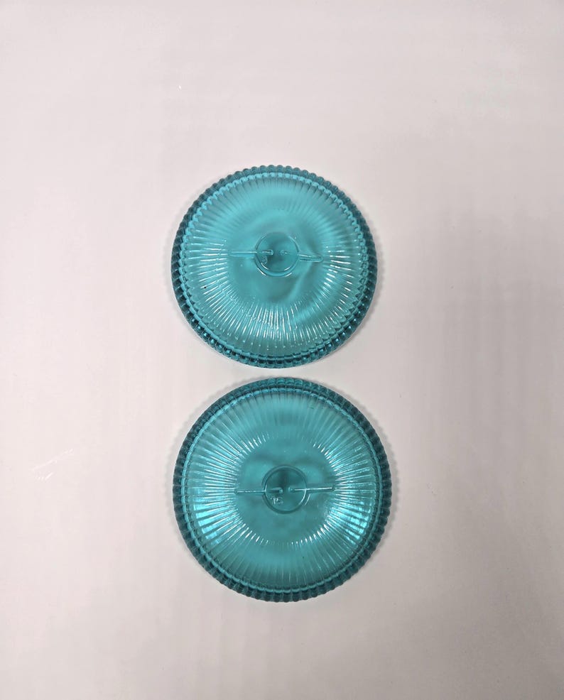May include: Two turquoise glass plates with a ribbed design and a beaded edge. The plates are round and have a central design element. The plates are displayed on a white background.