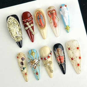 May include: A set of ten long, almond-shaped artificial nails. Each nail features unique religious-themed designs, including crosses, angels, and images of religious figures. The nails are adorned with gold, red, and blue embellishments.