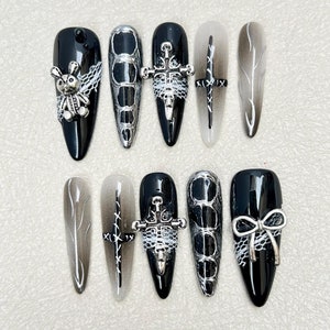 May include: Ten black and white nail designs featuring various silver accents. The designs include a spider, crosses, a feather, and a bow.